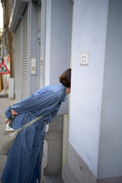 Woman in denim coat peering into a doorway on an urban street. Brussels, Belgium