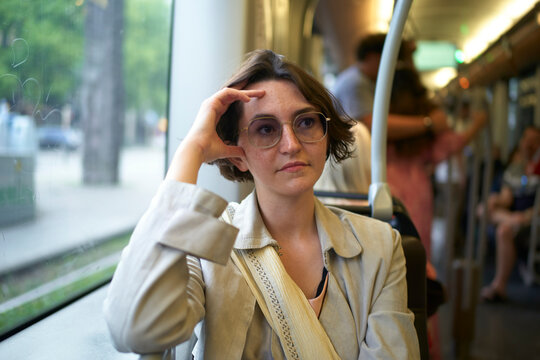 Young woman in light jacket sits on a train, gazing out the window thoughtfully. Brussels, Belgium