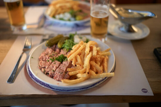 Plate of steak tartare with fries, pickles, and parsley garnish on a dining table. Brussels, Belgium