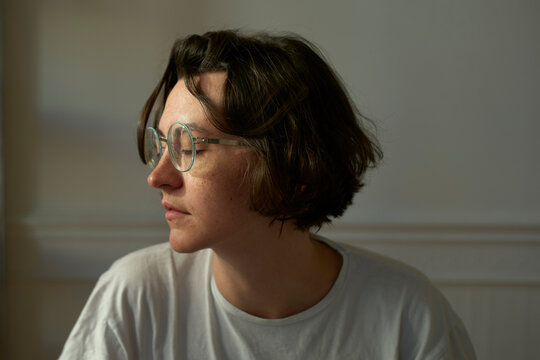 A woman in glasses with short hair looks to the side in a softly lit room. Brussels, Belgium