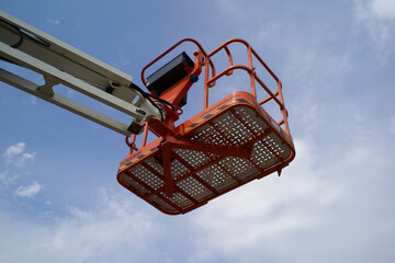 Orange cherry picker basket elevated against a clear blue sky with a few clouds. Germany