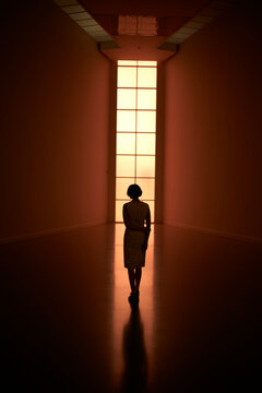 Silhouetted figure walking towards a large illuminated window in a dimly lit hallway. Germany