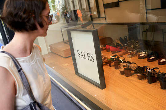 Woman looking at shoe display marked with sales sign in a store window. Germany