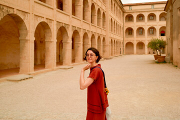 Woman in red dress walking through historic stone courtyard with arches and columns. Marseille, France