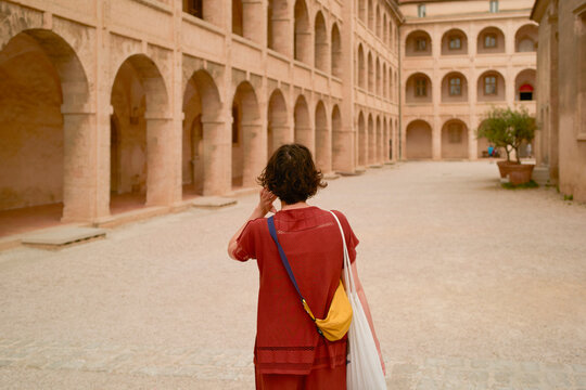 Woman in a red outfit walks through a historic courtyard with arches and soft lighting. Marseille, France