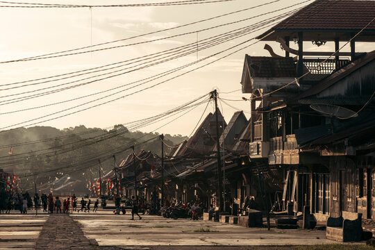 A bustling village street during sunset with silhouettes and distant mountains. Desa Hilisimaetano in South Nias, North Sumatra, Indonesia