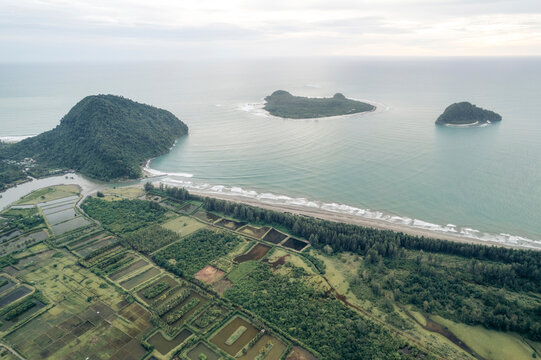 Aerial view of green farmland, forest, and ocean with small islands in the distance. Aceh Jaya Regency, Aceh, Sumatra, Indonesia