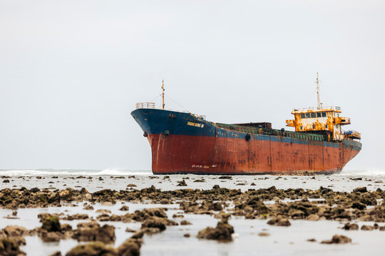Large rusted cargo ship stranded on a rocky shoreline under an overcast sky. Phan Rang, Ninh Thuan, Vietnam