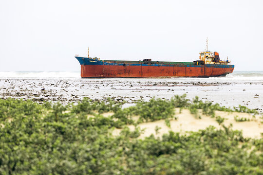 Rusty cargo ship stranded on a beach with green dunes in the foreground. Phan Rang, Ninh Thuan, Vietnam