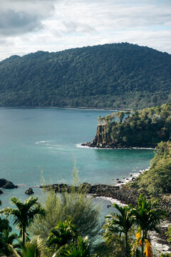 Lush island landscape with rocky cliffs and turquoise sea under a cloudy sky. Paya, on We Island in Aceh, Sumatra, Indonesia