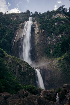 Majestic Air Terjun Nirwana Wartefall cascading down a lush, green mountain under a bright blue sky. Toba, North Sumatra, Indonesia