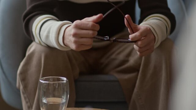 Cropped shot of unrecognizable patient holding eyeglasses in shaking hands feeling anxious sitting in front of healthcare specialist with clipboard in hands