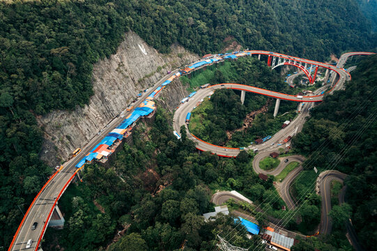 Aerial view of a winding mountain road with lush green forest and vibrant red bridges. Kelok 9, or the 9 hairpins, Harau, West Sumatra, Indonesia