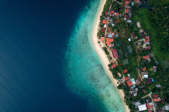 Aerial view of a coastal village with lush greenery and vibrant blue ocean. Sipora village area, Mentawai, West Sumatra, Indonesia
