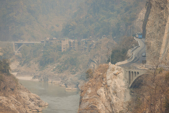 Mountain road curving along rocky cliffs with a river and distant village buildings. Road H05, Chandi Bhanjyang, Nepal