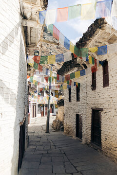 Narrow stone alleyway in a rustic village adorned with colorful prayer flags. Marpha, Annapurna, Mustang District of the Gandaki Province, Nepal