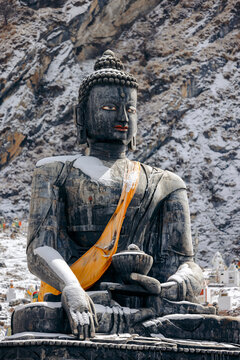 Snow-covered Buddha statue in front of a rocky mountain backdrop. Muktinath, Annapurna, Mustang District, Gandaki Province, Nepal