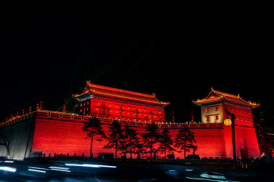 Ancient city wall illuminated in vivid red against a night sky, with dramatic lighting effects. Fortifications of Xi'an, China