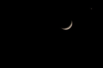 Crescent moon shining brightly against a dark night sky with a distant planet visible.