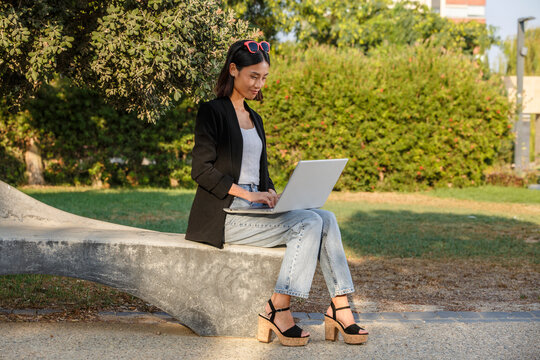 Woman sitting on outdoor bench using laptop on a sunny day in a park. Spain
