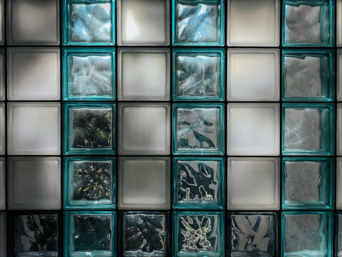 Patterned glass block wall with alternating frosted and textured transparent squares, creating a geometric and light-reflecting design. - Powered by Adobe