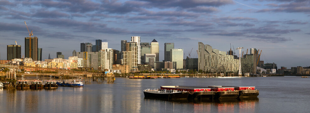 London skyline at sunset with skyscrapers and barges on the Thames River.