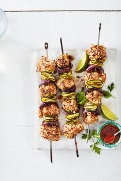 Grilled chicken skewers with zucchini, lime slices, and sauce on a white background.