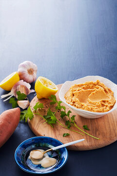 Spread of hummus, lemon, and garlic on a wooden board with a dark blue background.