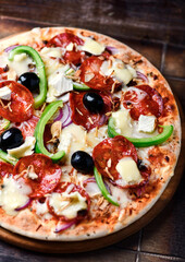 Pizza with chorizo ​​sausage, mozzarella cheese, green pepper and black olives. Rustic wooden background. Soft focus.	