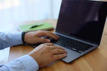 Man working on laptop at wooden table indoors, closeup