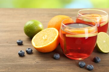 Tasty punch with fruits and blueberries on wooden table against blurred green background, closeup. Refreshing drink