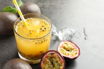Tasty passion fruit drink with ice cubes and fresh fruits on grey table, closeup. Space for text
