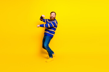 Cheerful young man with a red beard dancing playfully in a colorful outfit against a bright yellow background
