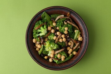 Delicious salad with shimeji mushrooms, chickpeas and broccoli in bowl on green background, top view