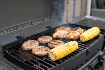 Grilled corn, chicken, and burgers cooking on a backyard bbq grill
