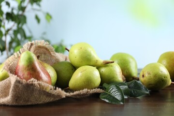 Fresh ripe pears on wooden table and green leaves outdoors, closeup