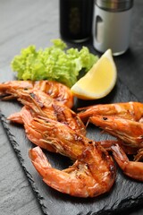 Tasty grilled shrimps with lemon and lettuce on black table, closeup. Delicious seafood dish