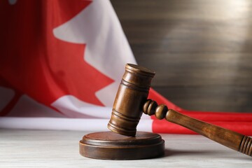 Judge's gavel on wooden table against flag of Canada, closeup