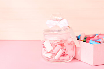Color paper pieces in box and glass jar on pink table, space for text