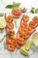 Skewers with tasty grilled shrimps, lime slices, herbs and sauce on white marble table, flat lay. Delicious seafood dish