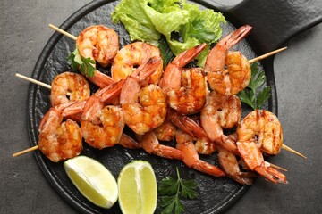 Skewers with tasty grilled shrimps, lime slices, parsley and lettuce on grey table, top view. Delicious seafood dish