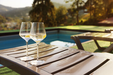 Glasses of wine on sun lounger near swimming pool outdoors, space for text