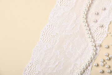 Beautiful pearls and lace fabric on beige background, flat lay
