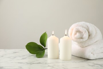 Burning candles, towels and leaves on white marble table, closeup. Space for text