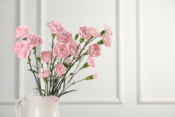 Beautiful carnation flowers in vase near white wall, closeup. Space for text