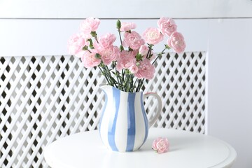 Beautiful carnation flowers in jug on white table indoors