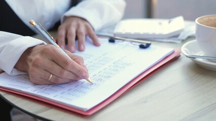 A focused businesswoman writes notes in a notebook at a cafe. She enjoys her coffee while planning and organizing her tasks in a serene setting, surrounded by a professional atmosphere