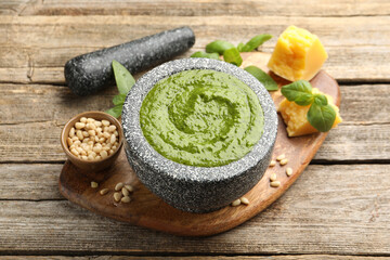 Tasty green pesto in mortar and ingredients on wooden table, closeup