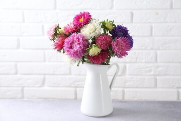 Beautiful flowers in vase on grey table near white brick wall indoors, closeup