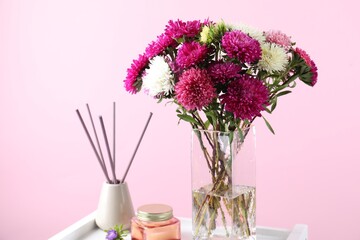 Beautiful flowers in vase, candle and incense sticks on white stand against pink background, closeup
